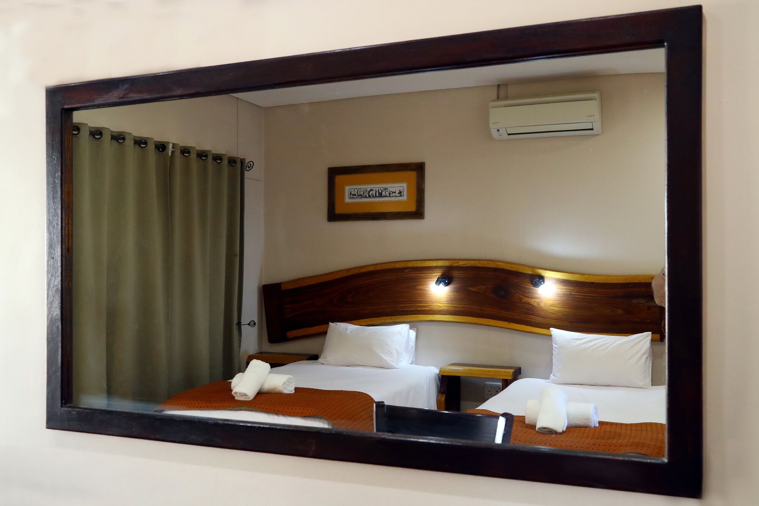 A hotel room with a large mirror, a bed with white linens, a wooden headboard, and a framed picture on the wall.