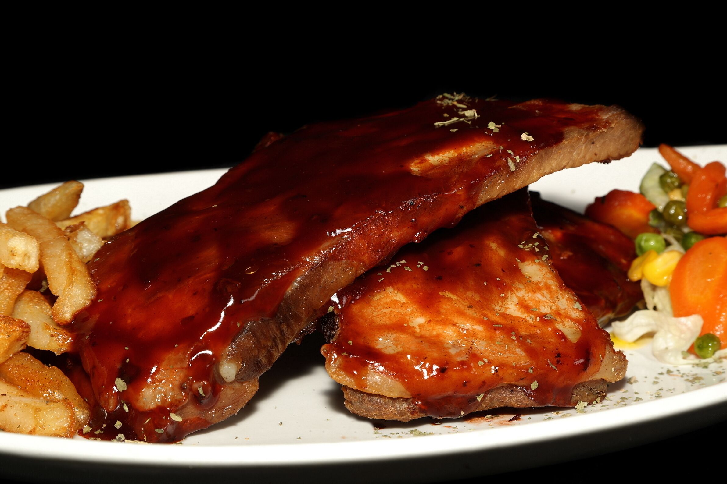 A plate with two pieces of meat covered in a glossy sauce, accompanied by a side of fries and mixed vegetables.