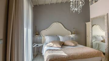 A bedroom with a large bed, a chandelier, a nightstand, and a mirror.