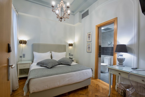 A bedroom with a bed, bedside tables, a desk, a chair, a chandelier, and a mirror.