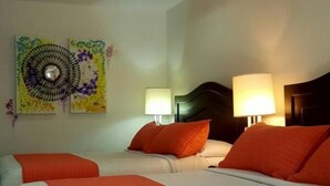 Ein Hotelzimmer mit zwei Betten, jedes mit weißer Bettdecke und orangefarbenen Kissen. Es gibt zwei Wandlampen und eine Deckenleuchte.