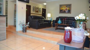 Eine Lobby mit einem schwarzen Ledersofa, einem Couchtisch, einem an der Wand montierten Fernseher und einer Vase mit weißen Blumen auf einem Tisch.