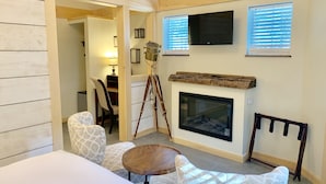 A cozy room with a fireplace, a mounted TV, and a wooden ceiling. - Ivy Manor Inn Village Center (Bar Harbor)
