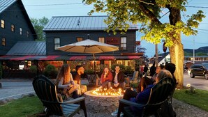 A group of people sitting around a fire pit in an outdoor setting with a building in the background. - Ivy Manor Inn Village Center (Bar Harbor)