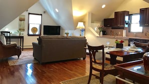 A spacious living area with a high ceiling, wooden flooring, a sofa, a dining table, and a kitchen in the background. - Ivy Manor Inn Village Center (Bar Harbor)
