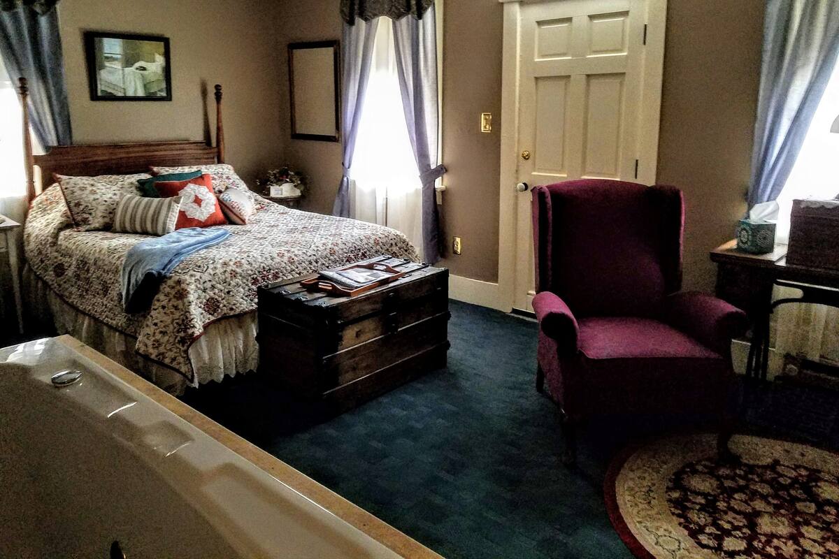A bedroom with a bed, a chair, a dresser, and a door.