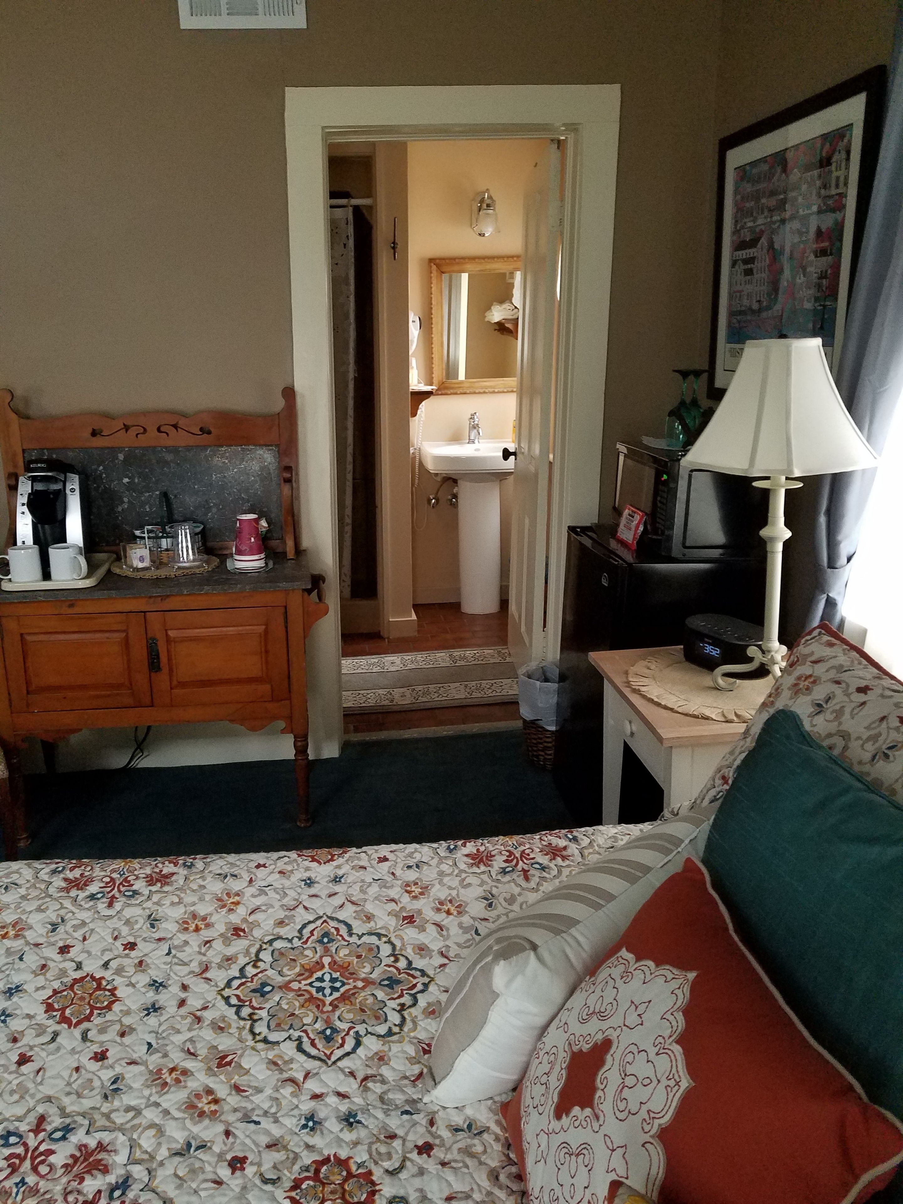 A hotel room with a bed, a desk with a lamp, a coffee maker, and a TV.