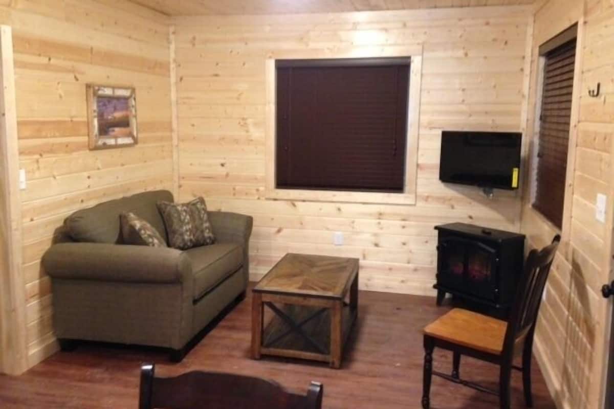A cozy cabin interior with a sofa, a coffee table, a chair, and a television mounted on the wall.