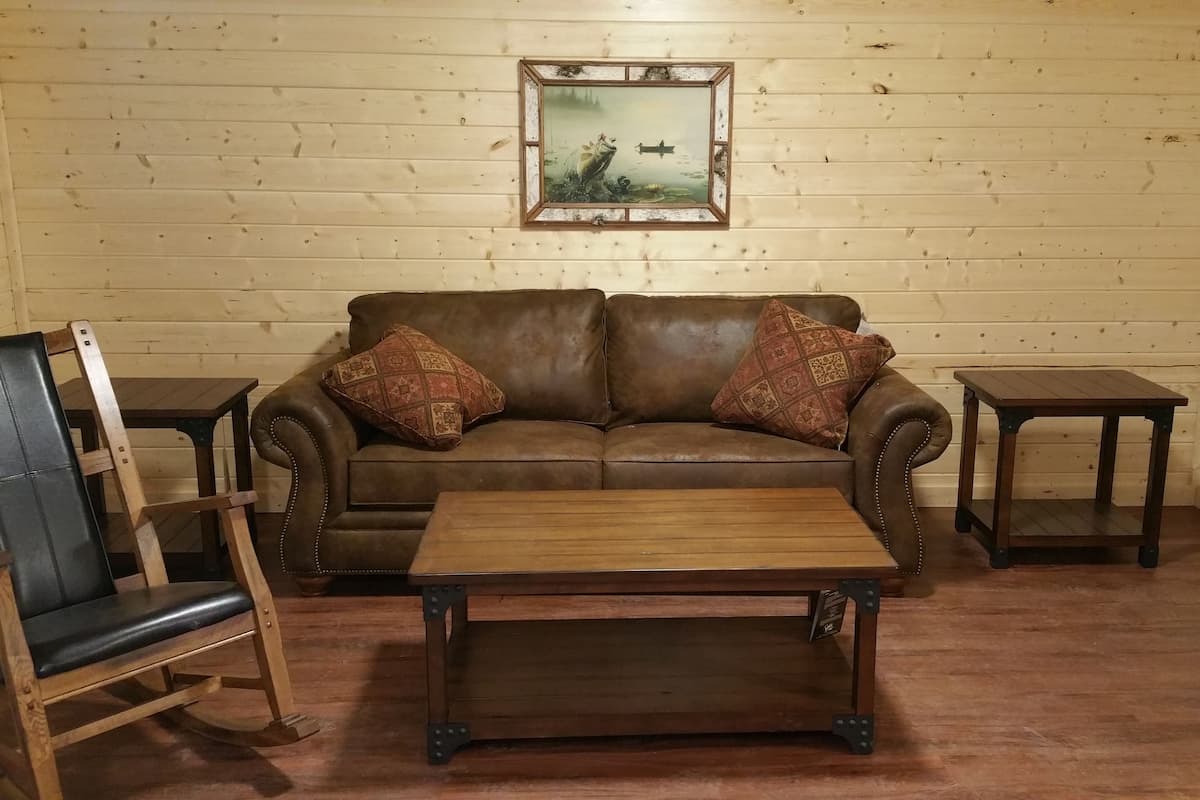A cozy room with a brown leather sofa, two matching armchairs, a wooden coffee table, and a framed picture on the wall.