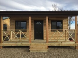 Una cabaña de madera con un porche, una puerta negra y el número '3' en la fachada.