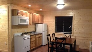 A compact kitchen with wooden cabinets, a microwave, a stove, a refrigerator, and a dining table with chairs.