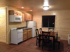 Una cocina compacta con armarios de madera, microondas, estufa, refrigerador y una mesa de comedor con sillas.