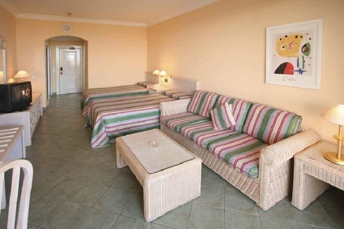 Une chambre d’hôtel avec deux lits simples, un canapé, une petite table et un téléviseur.