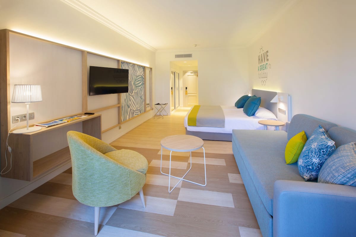 Une chambre d’hôtel moderne équipée d’un téléviseur à écran plat, d’un canapé, d’un fauteuil, d’un lit et d’une petite table.