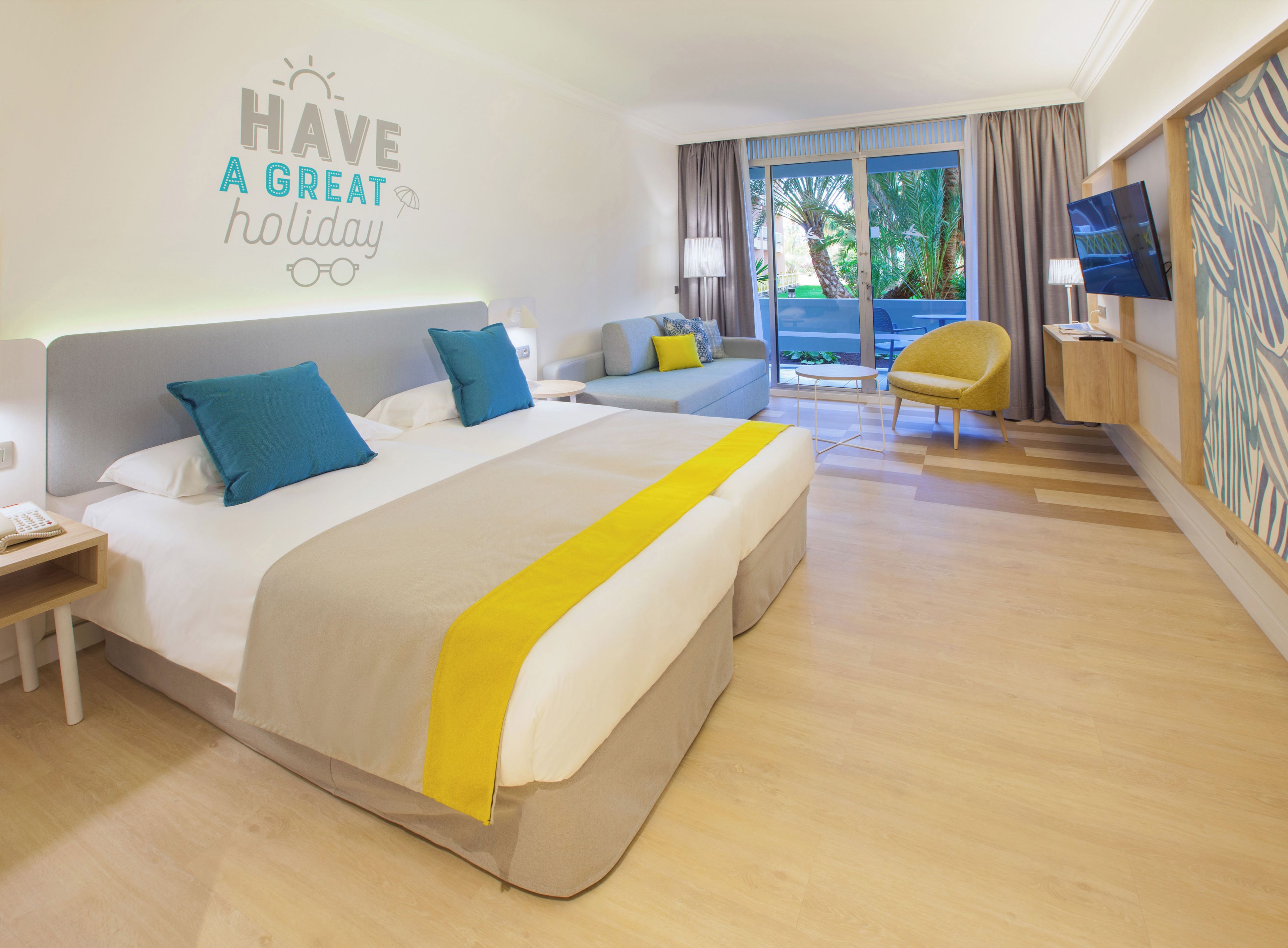 Habitación de hotel con una cama grande, un sofá, una silla, un televisor y un balcón con cortinas.