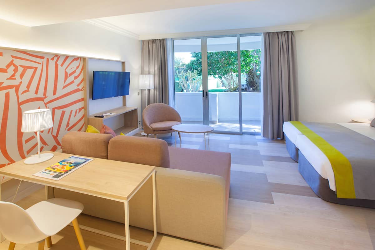 Une chambre d’hôtel moderne équipée d’un canapé, d’une petite table, d’une télévision et d’un balcon avec des rideaux.
