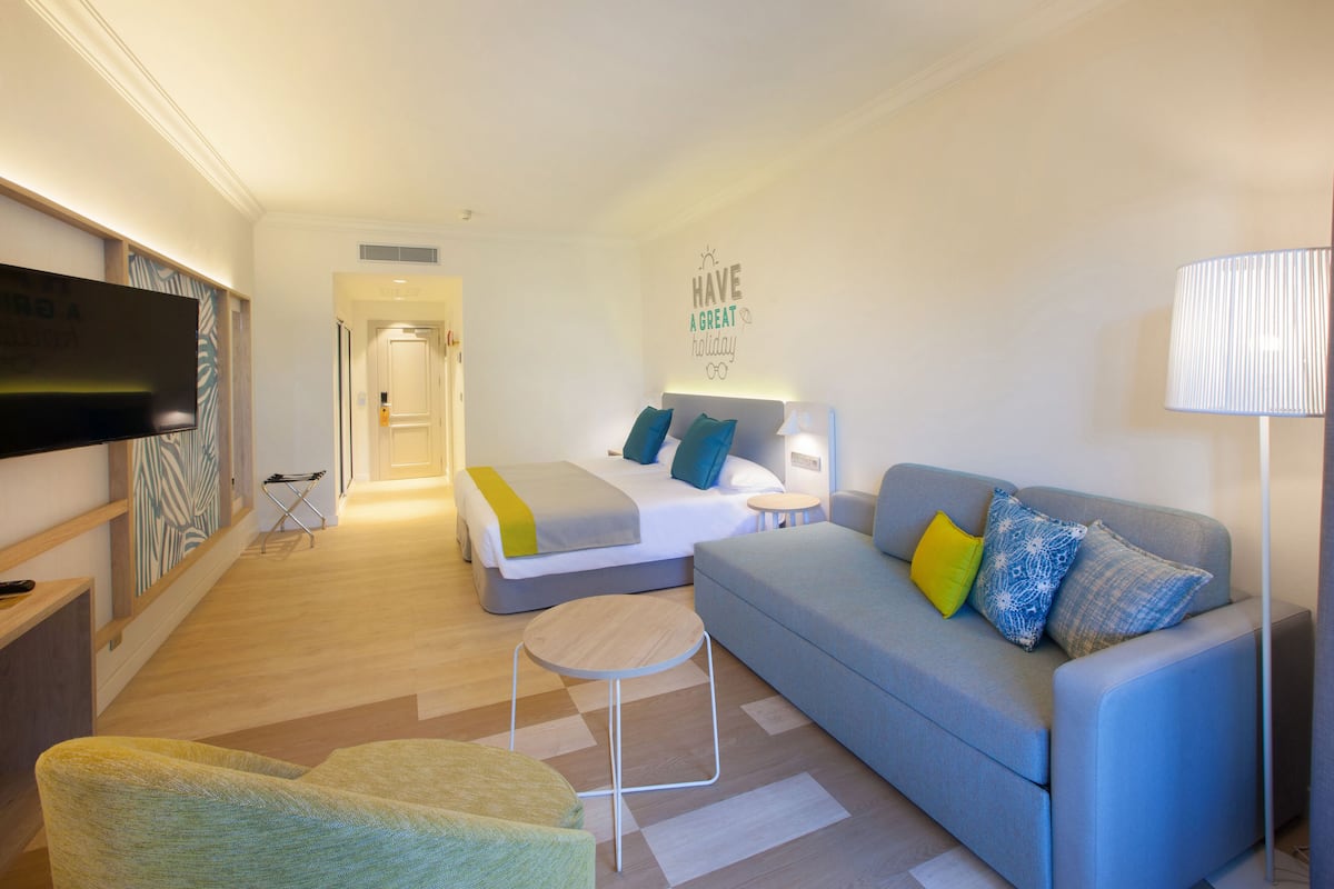 Une chambre d’hôtel moderne équipée d’un lit, d’un canapé, d’une télévision et d’un mur orné d’un message de circonstance.