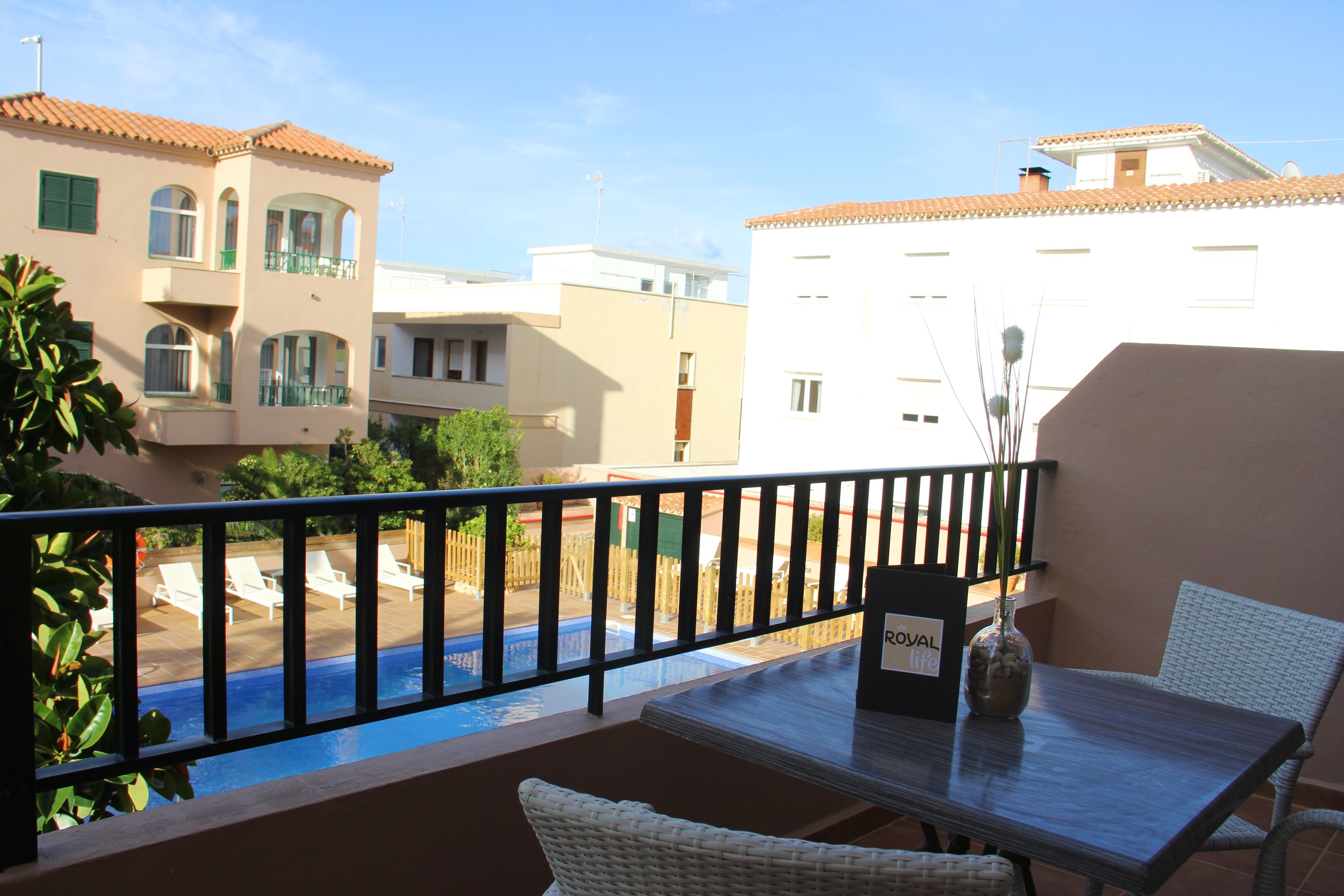 A balcony with a view of a swimming pool, a table with a vase, and a wicker chair.
