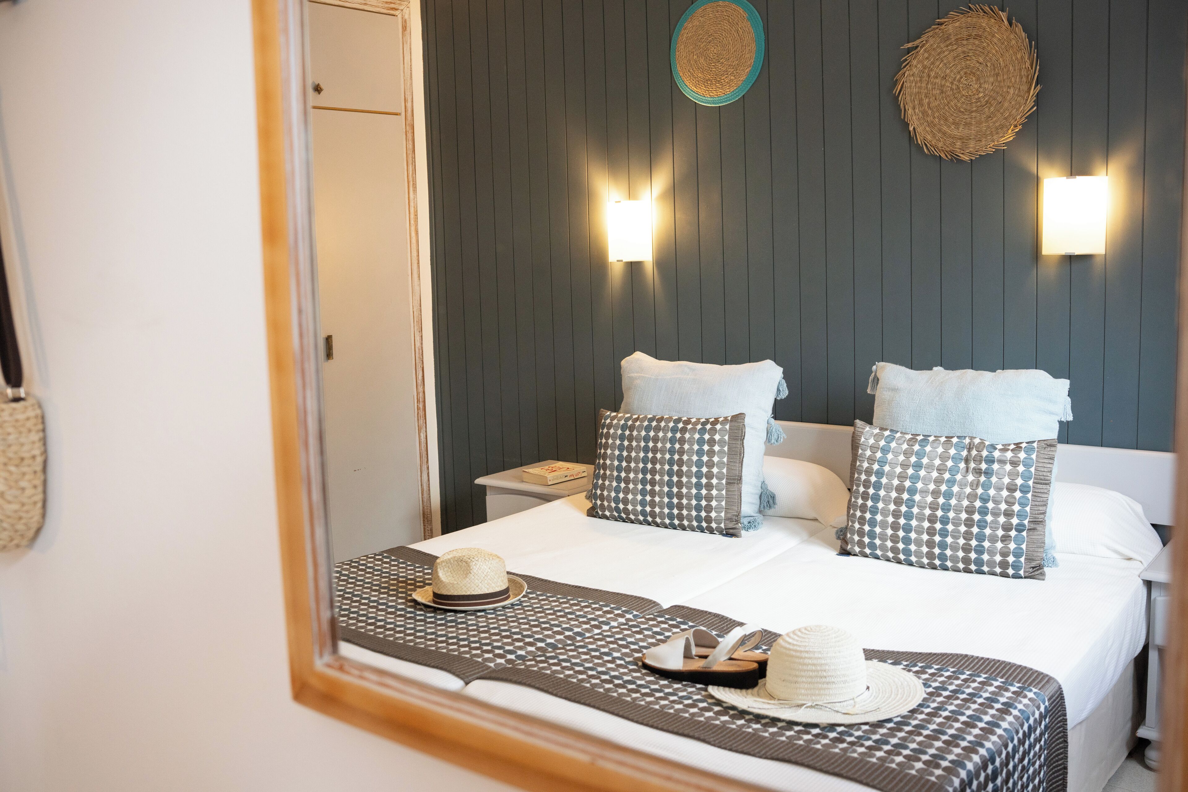 A neatly made bed with a patterned bedspread, two pillows, and a hat on the bed.