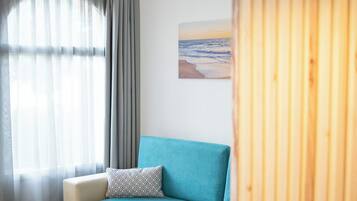 A cozy living room with a teal sofa, a wooden dining table with chairs, a coffee table, and a pendant light.