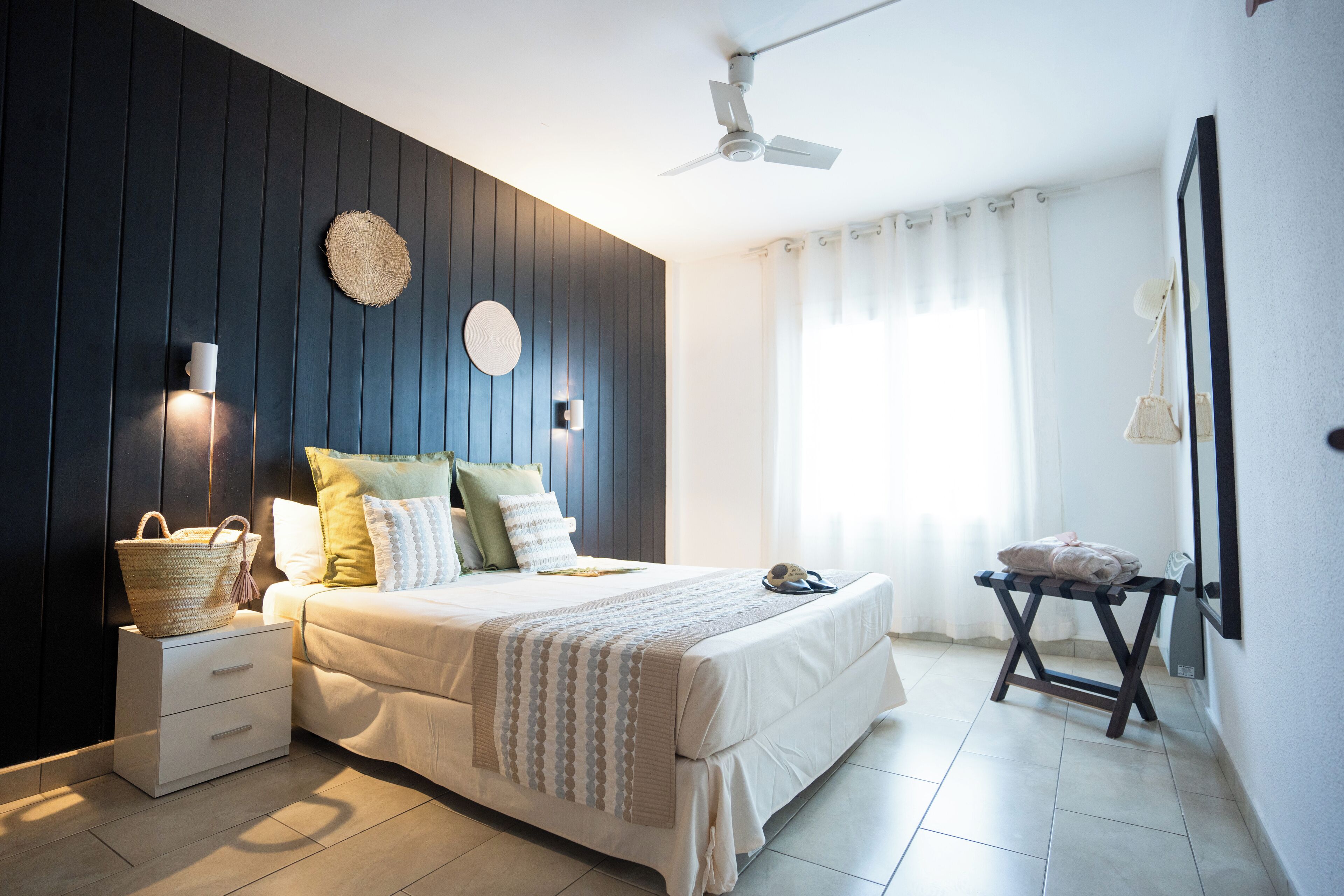 A bedroom with a bed, bedside tables, a ceiling fan, and a window with curtains.
