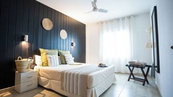 Un dormitorio con cama, mesitas de noche, ventilador de techo y ventana con cortinas.
