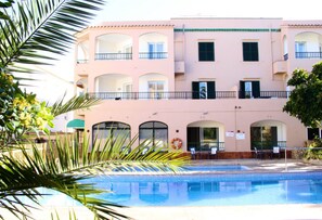 A multi-story hotel with a pool area, balconies, and a palm tree in the foreground. - Apartamentos Royal Life (Mahón)