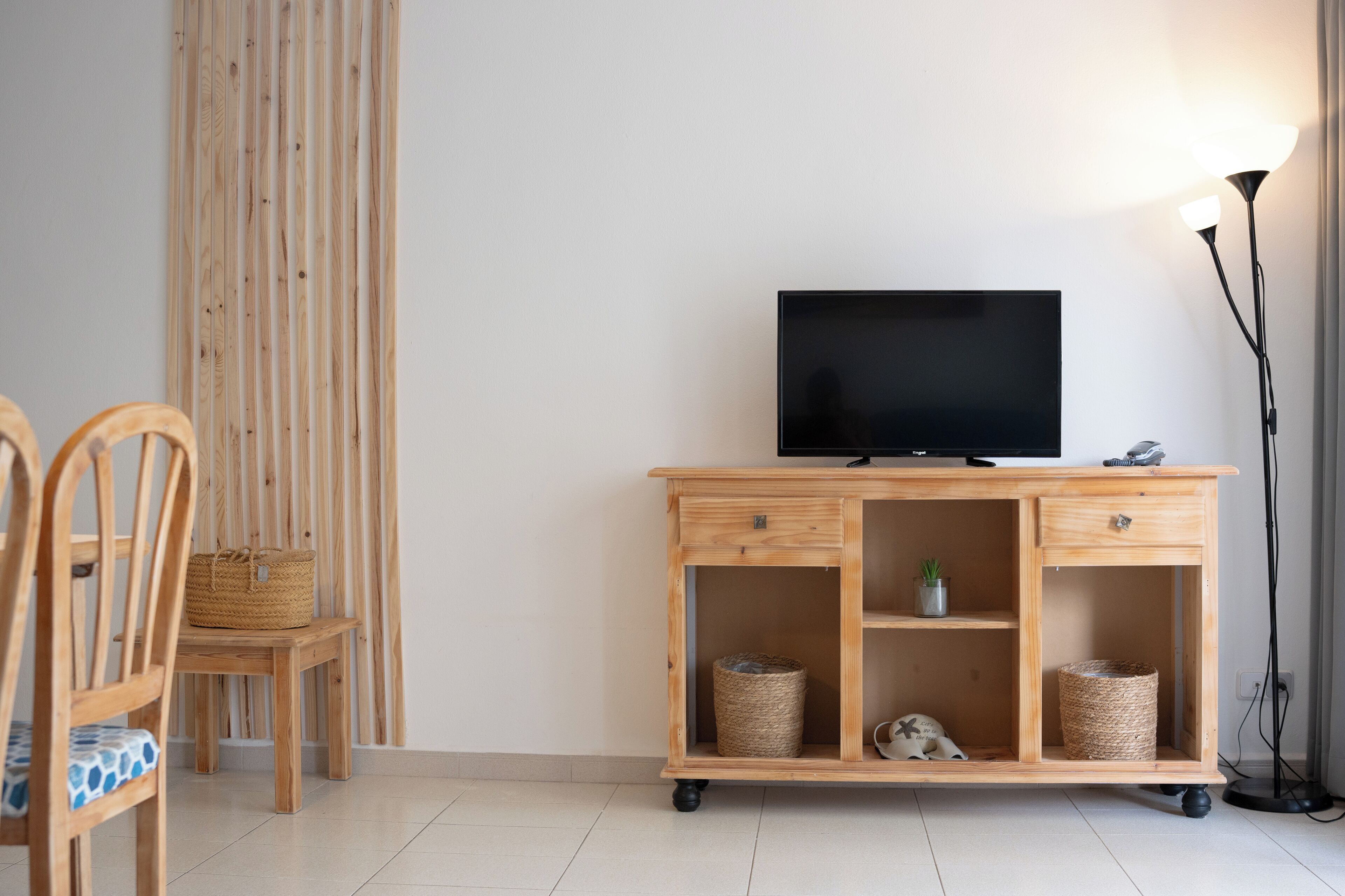 A wooden TV stand with a flat-screen TV, two wicker baskets, and a lamp.