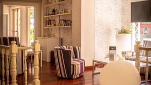 A living room with a wooden staircase, a striped armchair, a round white ottoman, and a bookshelf. - Apartamentos Royal Life (Mahón)