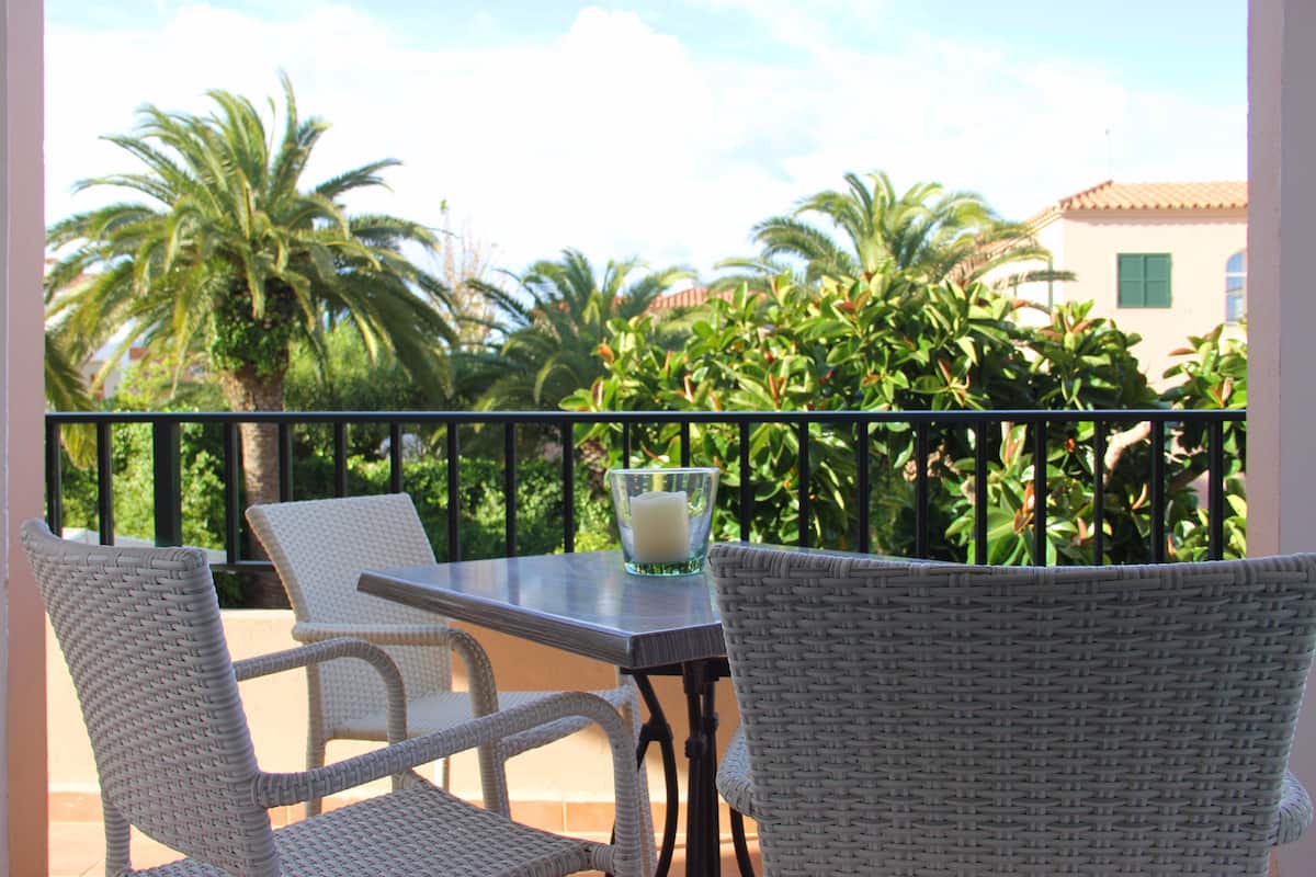 A balcony with wicker chairs, a table, and a glass candle holder.