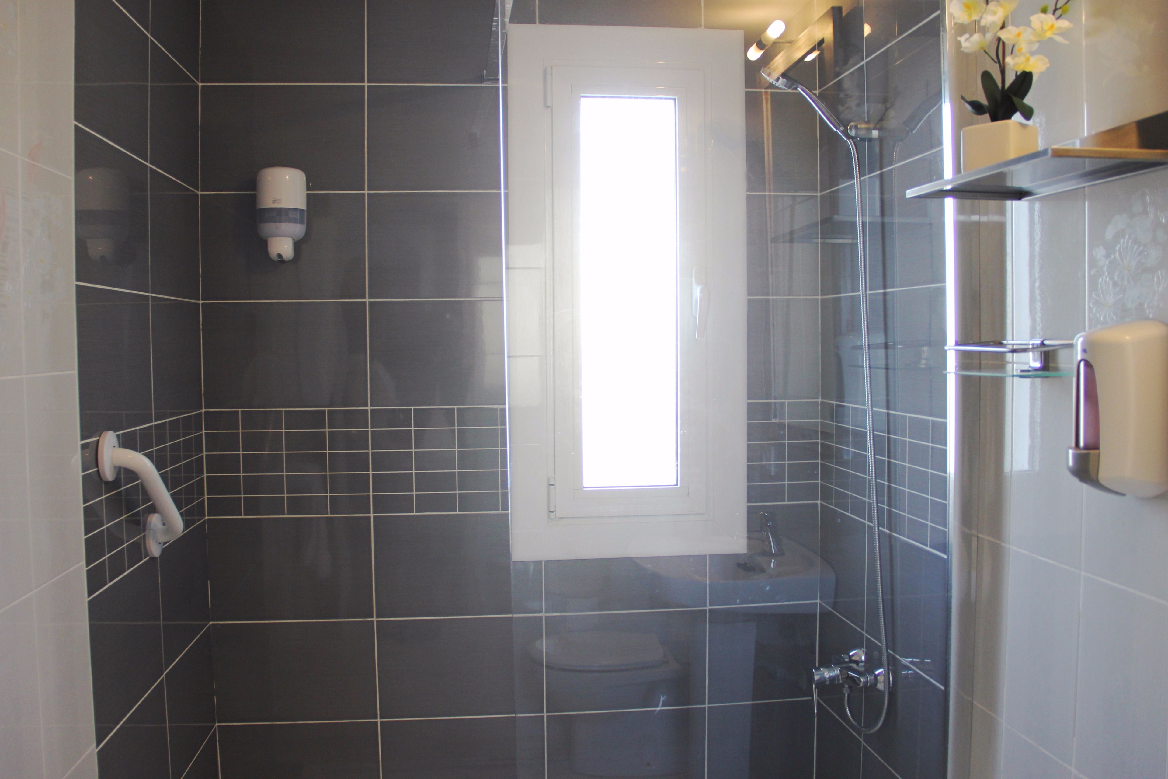 A bathroom with dark tiles, a toilet, a shower, and a small window.