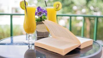 Dos vasos de jugo de naranja con limón y rodajas de kiwi, un libro y un florero con flores sobre una mesa de vidrio.