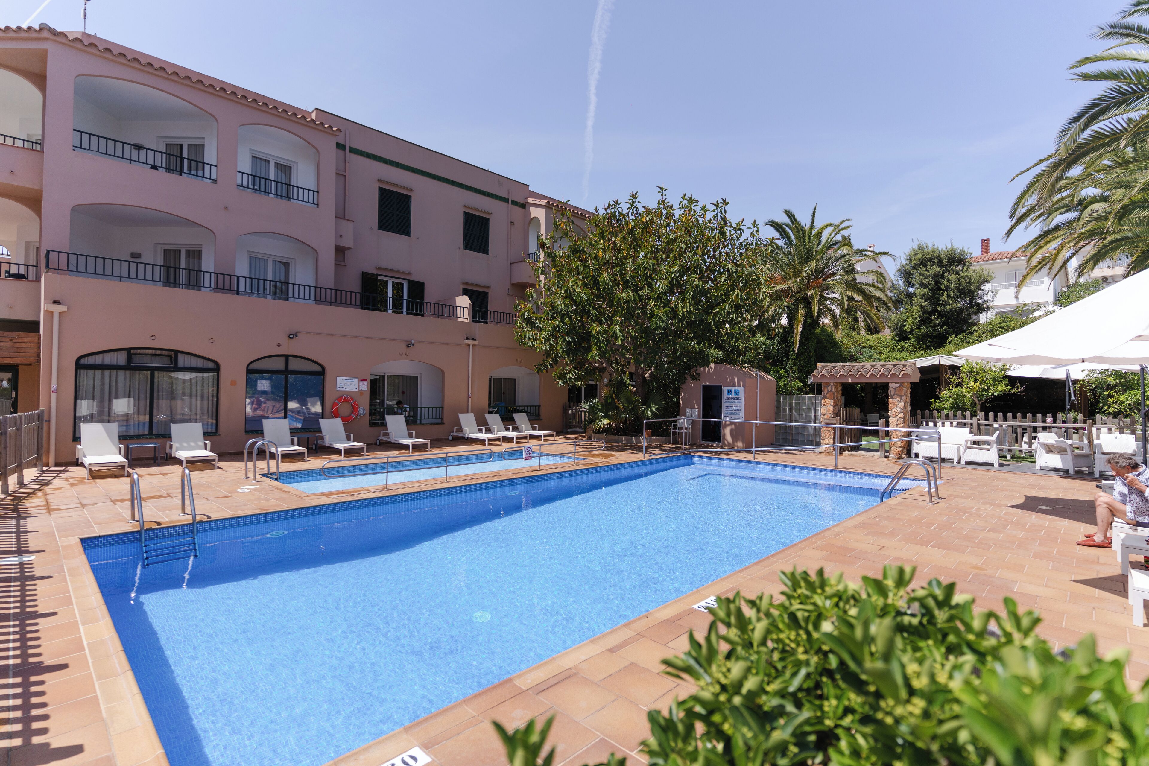 A swimming pool with lounge chairs, a building with balconies, and palm trees.