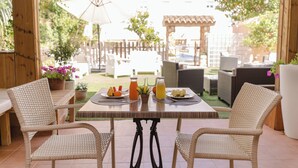 An outdoor patio with wicker chairs and a table set for two, featuring a drink and fruit. - Apartamentos Royal Life (Mahón)