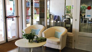 A reception area with two armchairs, a small table with a plant, and a glass door leading to a dining area. - Apartamentos Royal Life (Mahón)