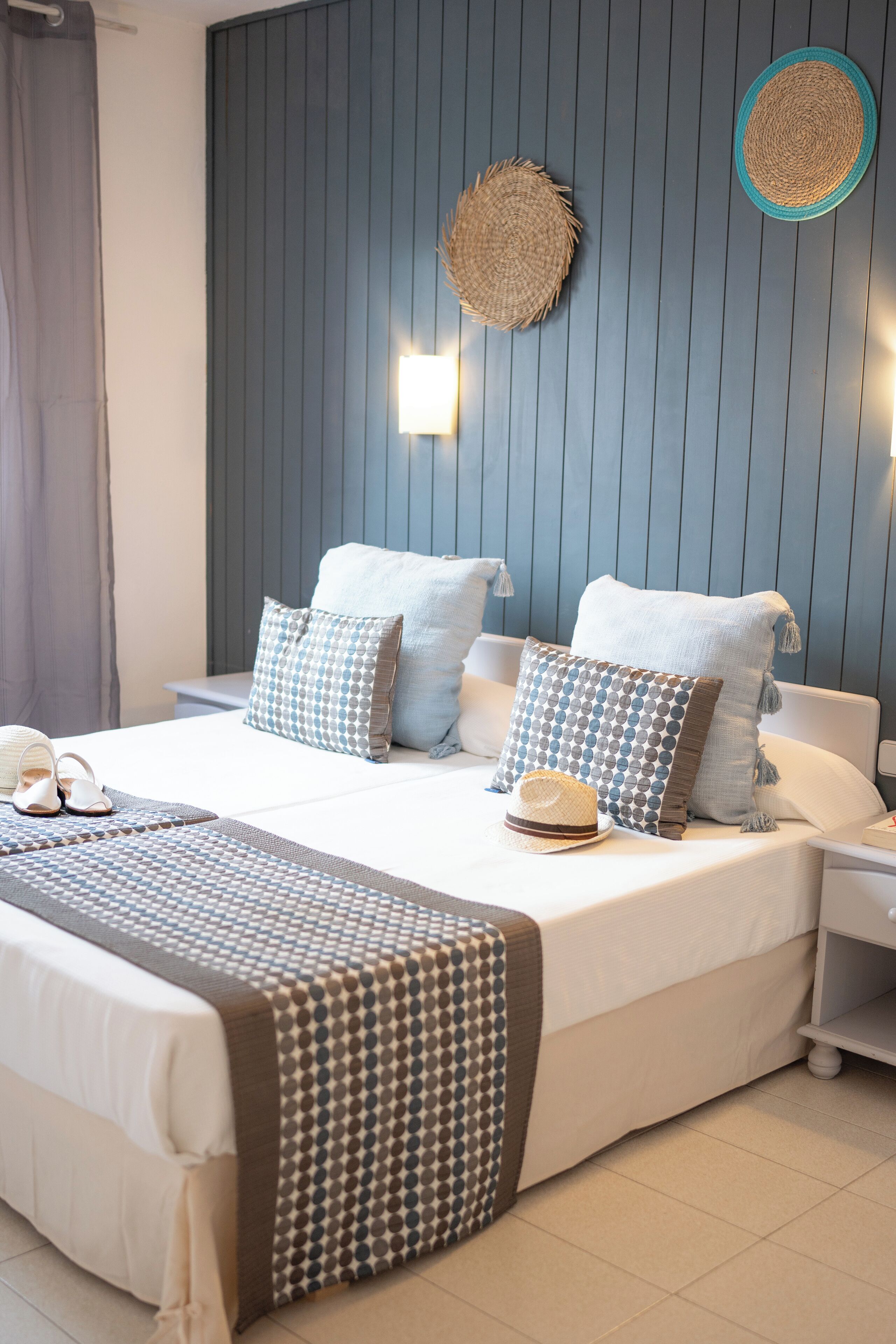 Una cama bien hecha con ropa de cama estampada, una mesita de noche y una lámpara de pared.