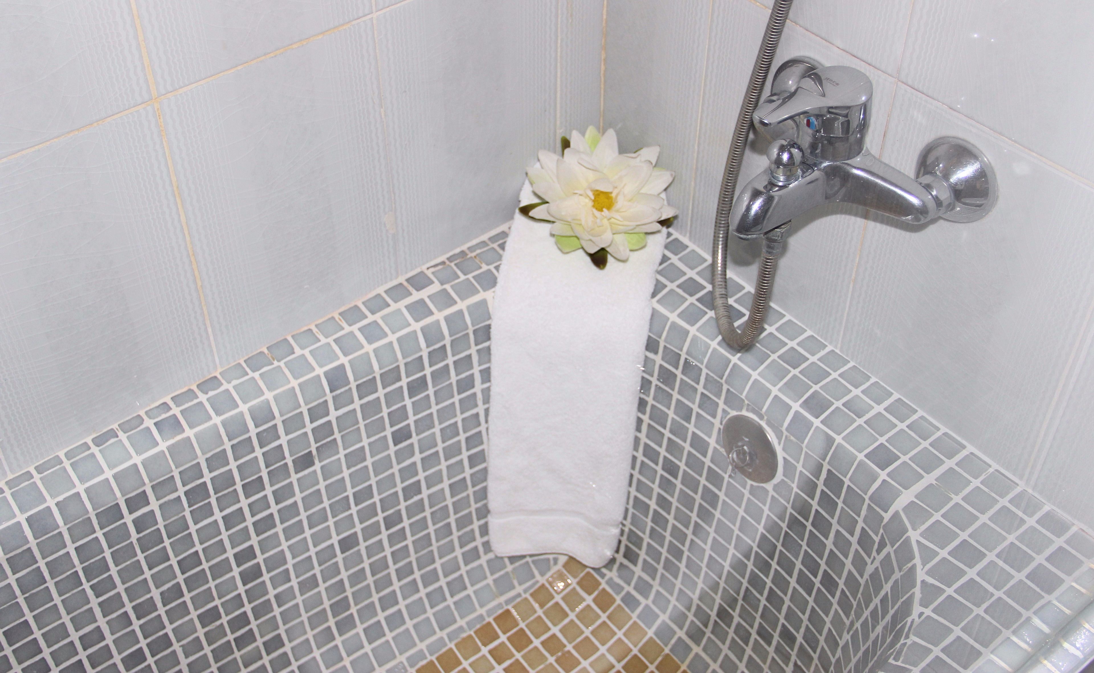 A bathroom with a white bathtub, a shower, and a towel rack with a white towel and a flower.
