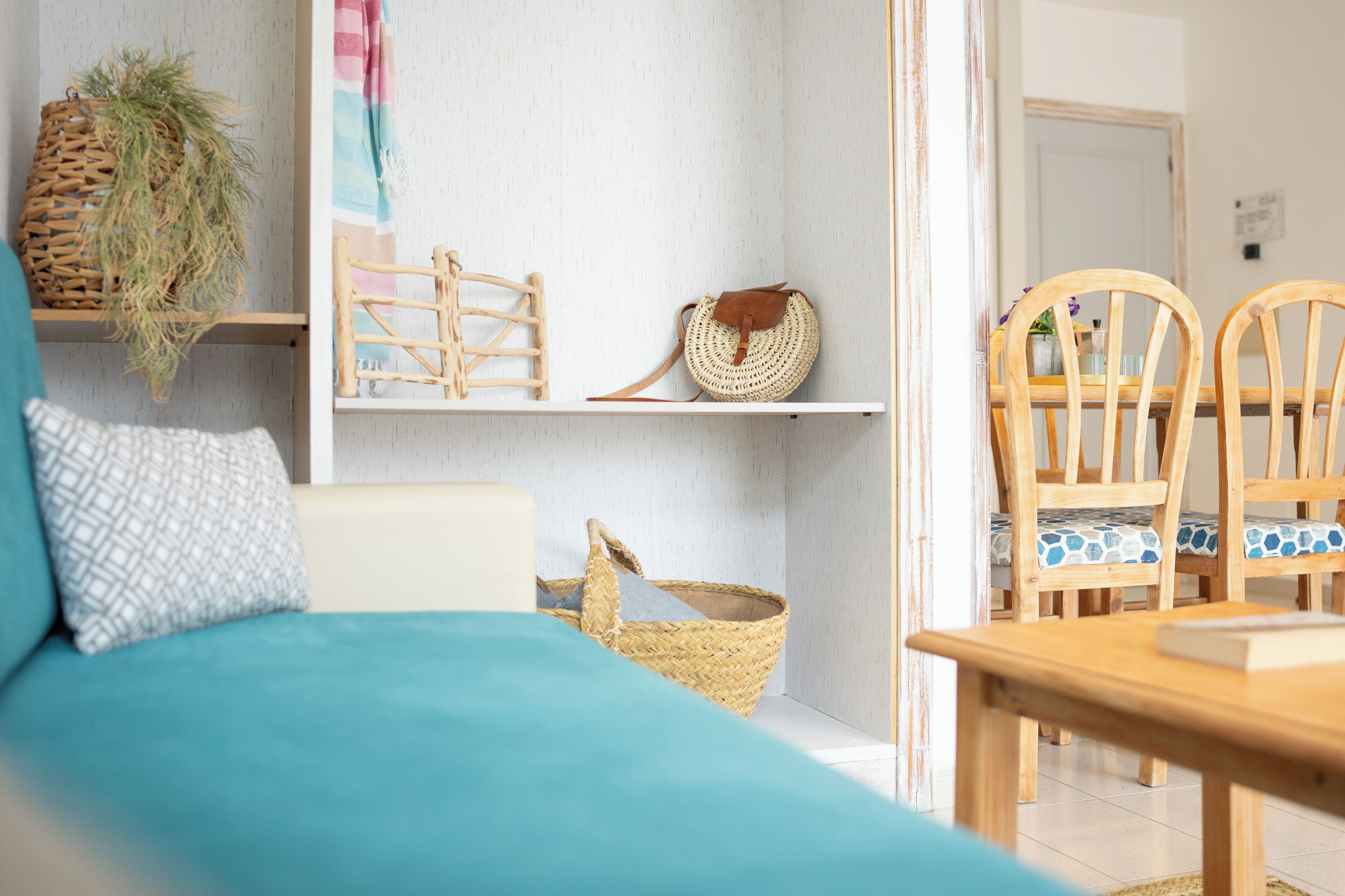 Une pièce avec un canapé de couleur turquoise, une table à manger en bois et des chaises. On y trouve des étagères avec des paniers et un sac en osier.