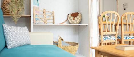 A room with a teal sofa, a wooden dining table, and chairs. There are shelves with baskets and a woven bag.