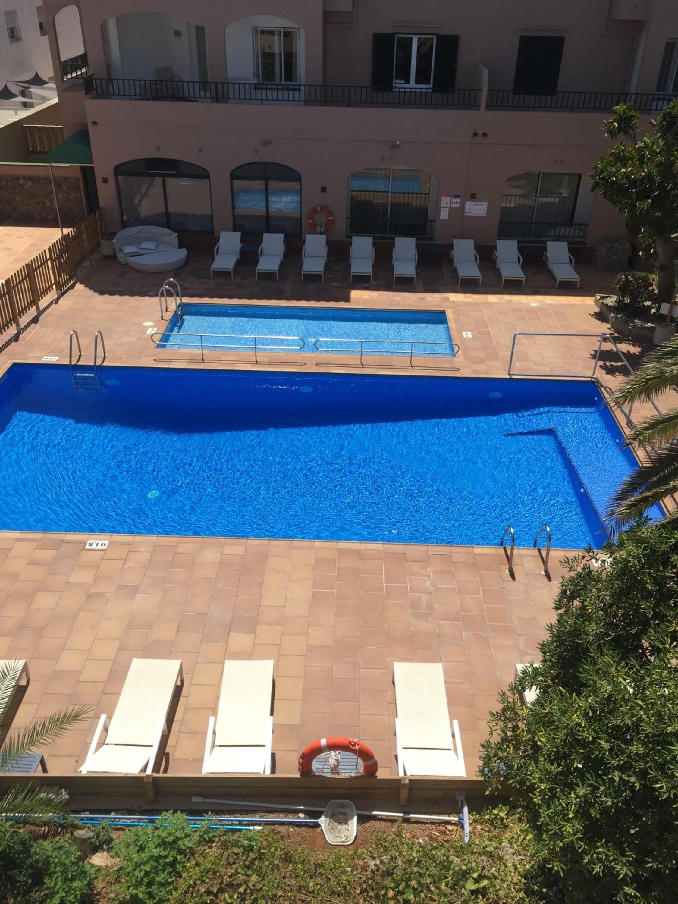 Una piscina al terrat amb dues zones, envoltada de gandules i un edifici amb balcons.