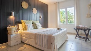 A bedroom with a bed, bedside tables, a window with a view, and a ceiling fan. - Apartamentos Royal Life (Mahón)