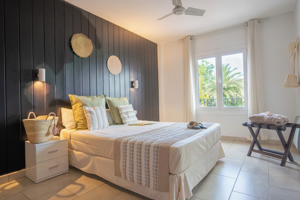 A bedroom with a bed, bedside tables, a window with a view, and a ceiling fan.