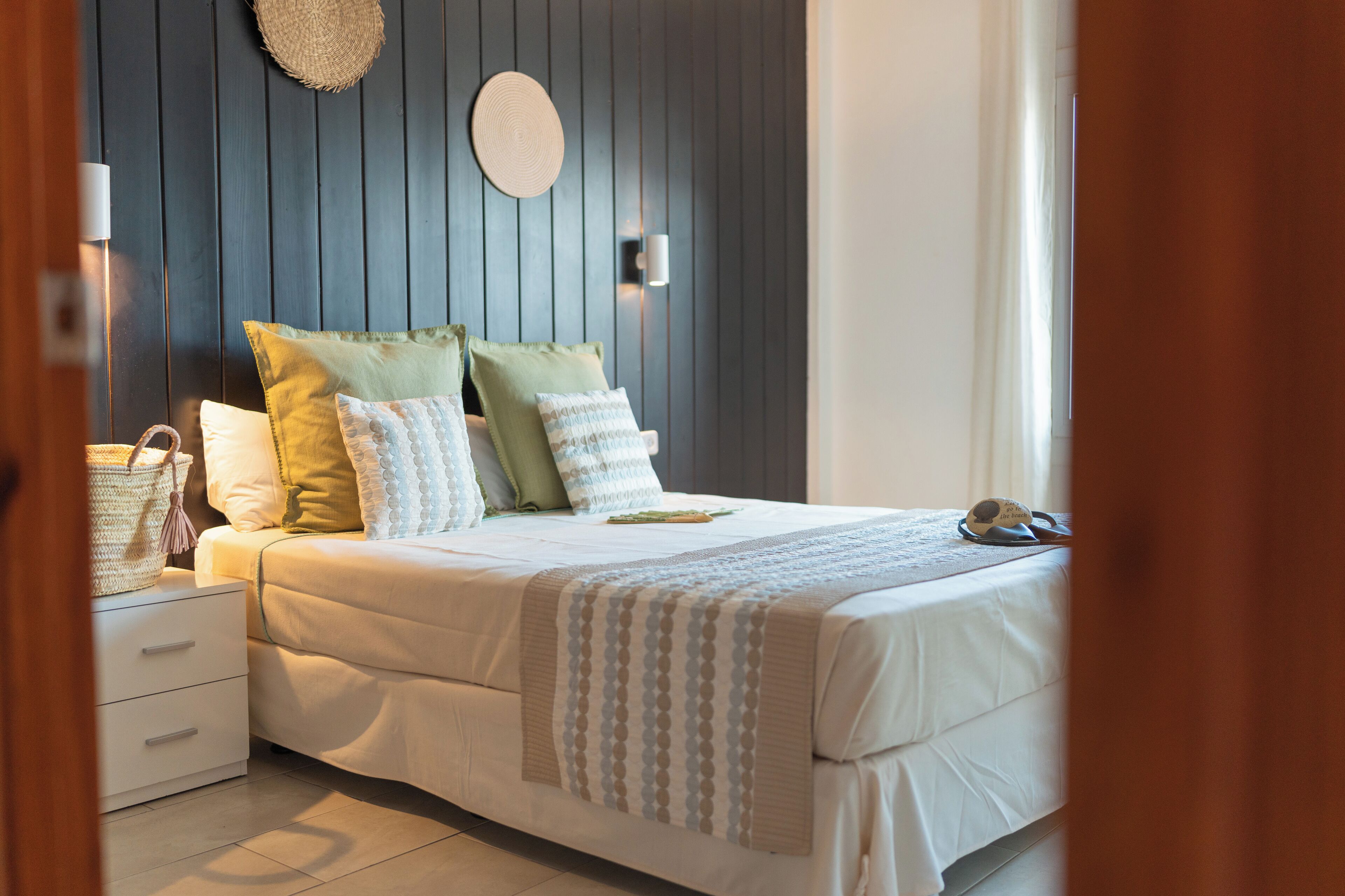 A neatly made bed with a striped blanket, a bedside lamp, and a wall-mounted round mirror.