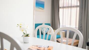 Une table à manger avec un magazine, une orchidée en pot et des chaises blanches.