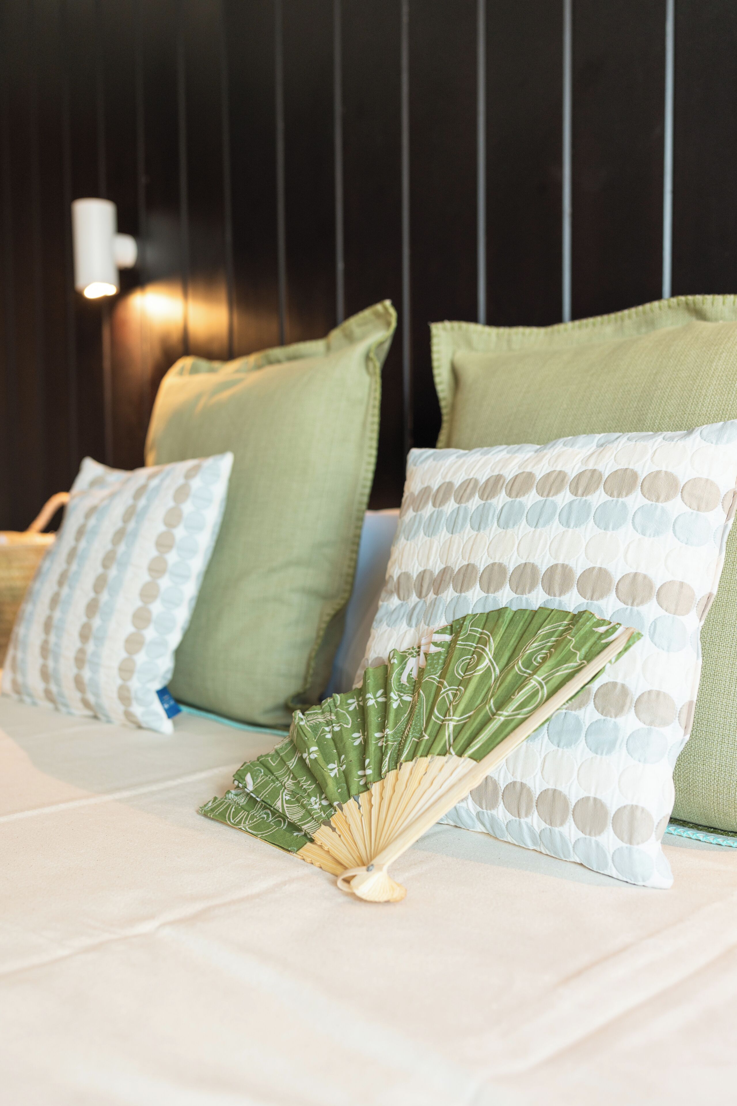 Una cama con almohadas verdes y blancas, un ventilador y un aplique de pared.