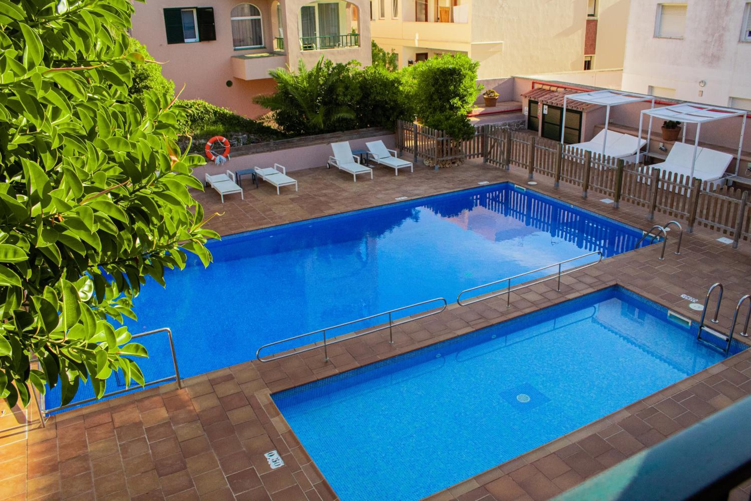 A rectangular swimming pool with a tiled deck, surrounded by lounge chairs and a wooden fence.