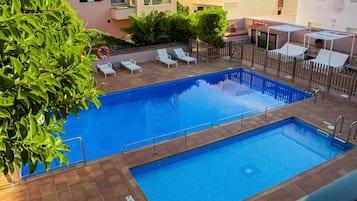 A rectangular swimming pool with a tiled deck, surrounded by lounge chairs and a wooden fence.