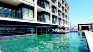 A swimming pool with lounge chairs and a building with multiple balconies. - FERGUS Cap Roig (L'Ampolla)
