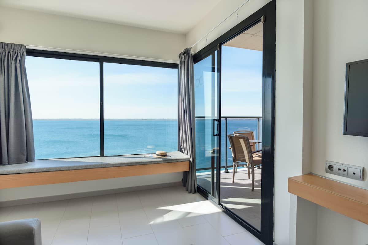 A balcony with a view of the sea, a window seat, and a table with chairs.
