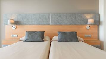 Cama doble con dos almohadas, cabecero con lámpara y mesita de noche con lámpara.